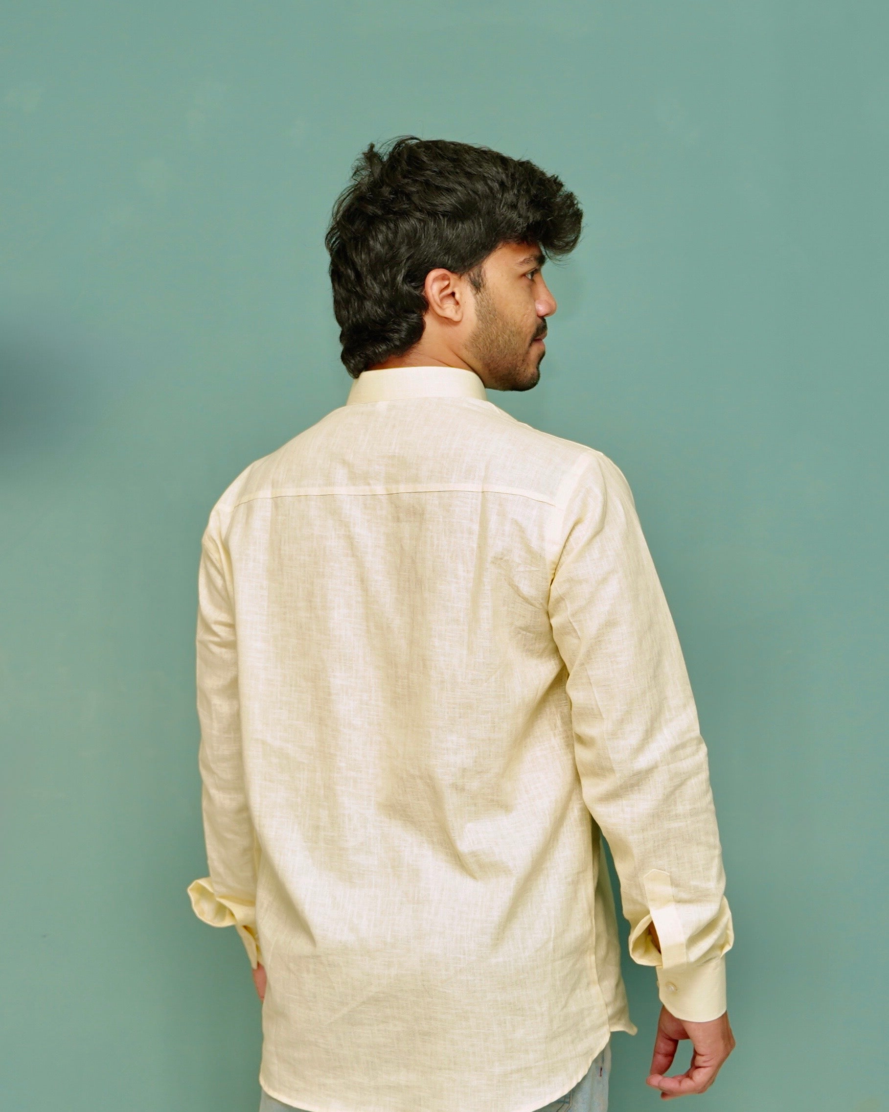 A man viewed from the back wearing a light cream-colored linen shirt against a solid teal background.