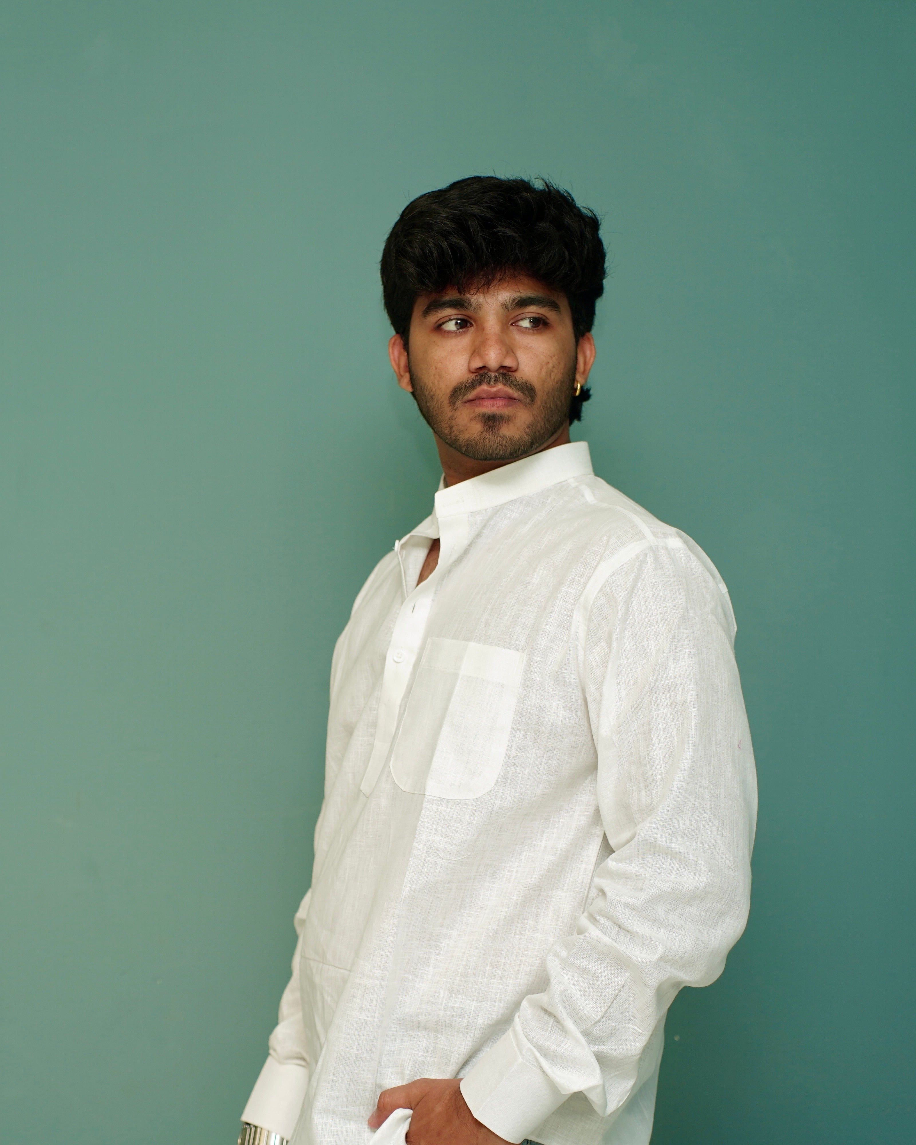 A man wearing a white long-sleeve textured shirt, standing against a solid teal-green background.