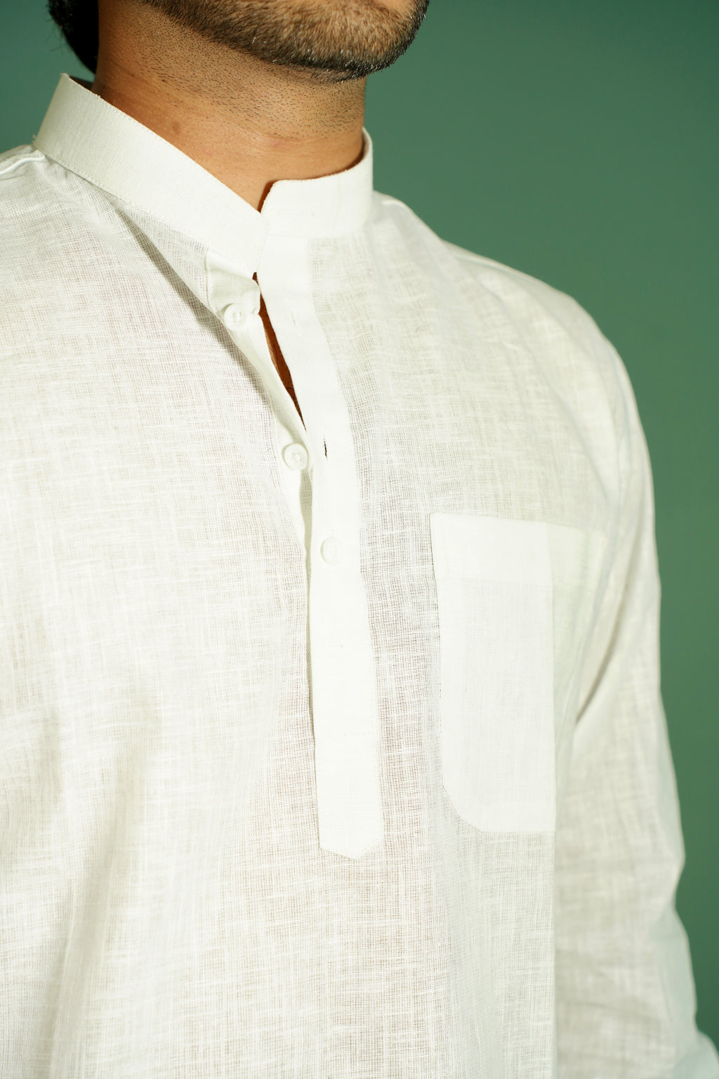 A close-up of a man wearing a white linen mandarin collar shirt with a button placket and a chest pocket, set against a solid green background.
