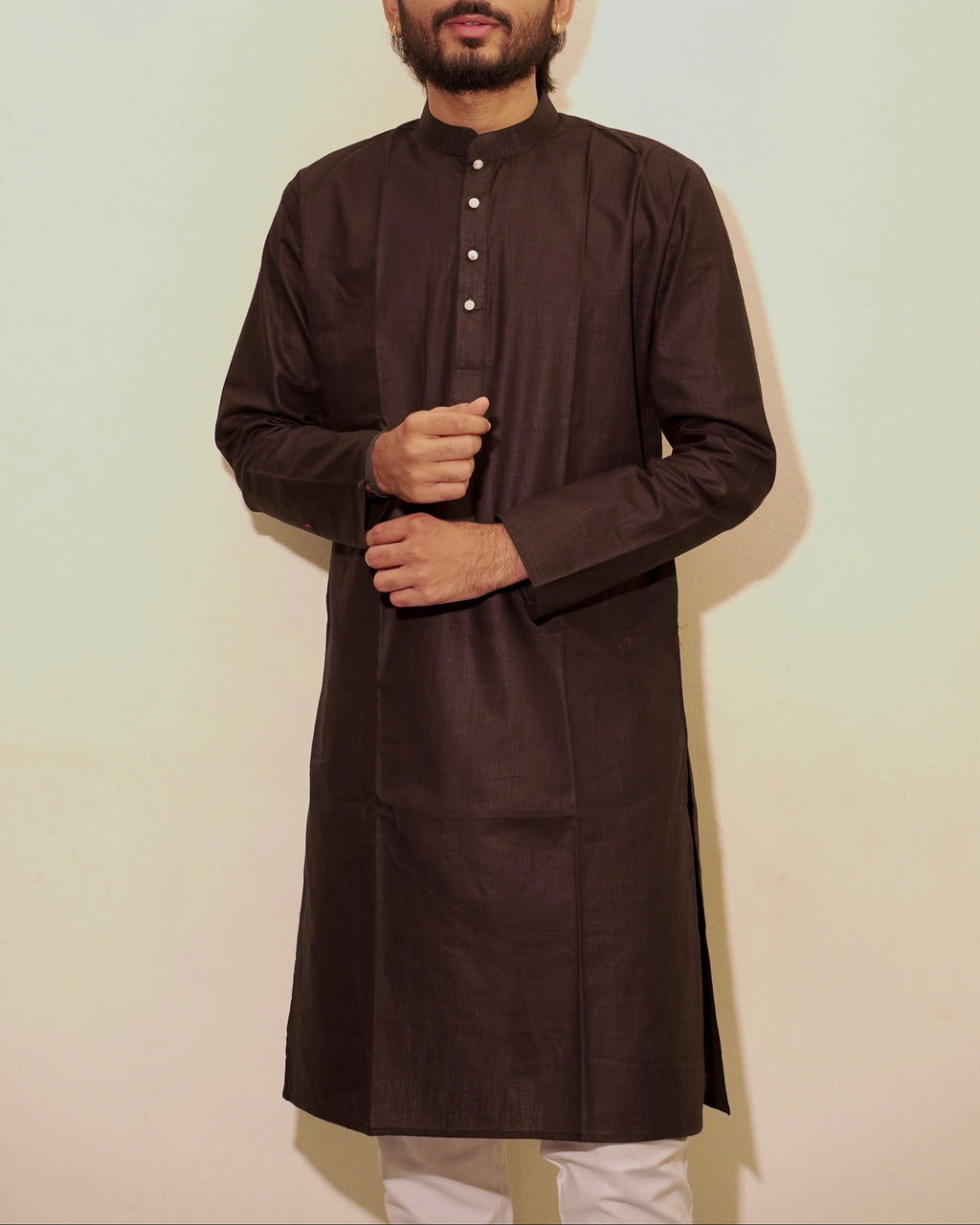 A man wearing a Black long-sleeved kurta with a mandarin collar and a buttoned placket, paired with white pajama, standing against a plain off-white background.