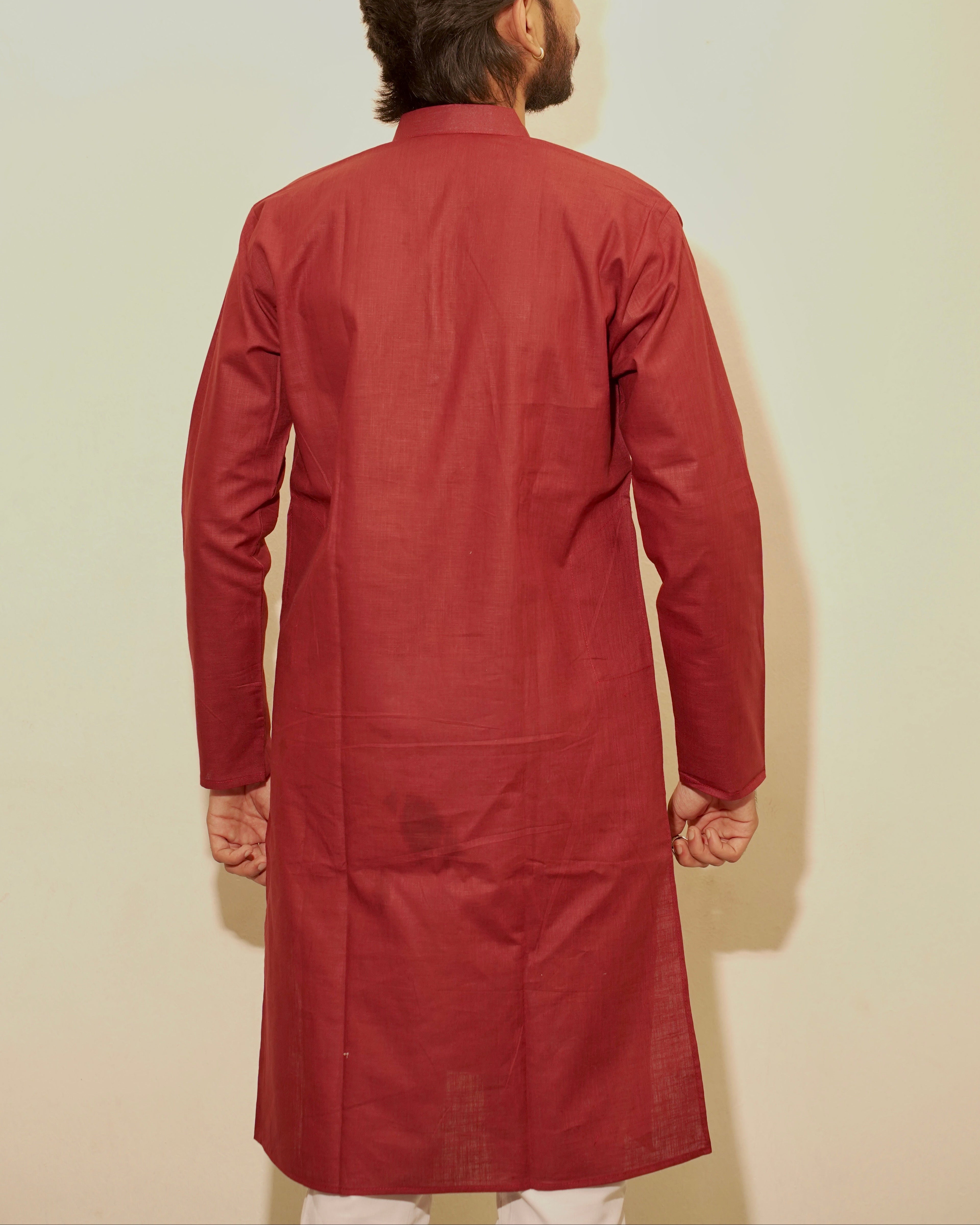 A man viewed from behind wearing a long-sleeved maroon kurta against a plain off-white background.