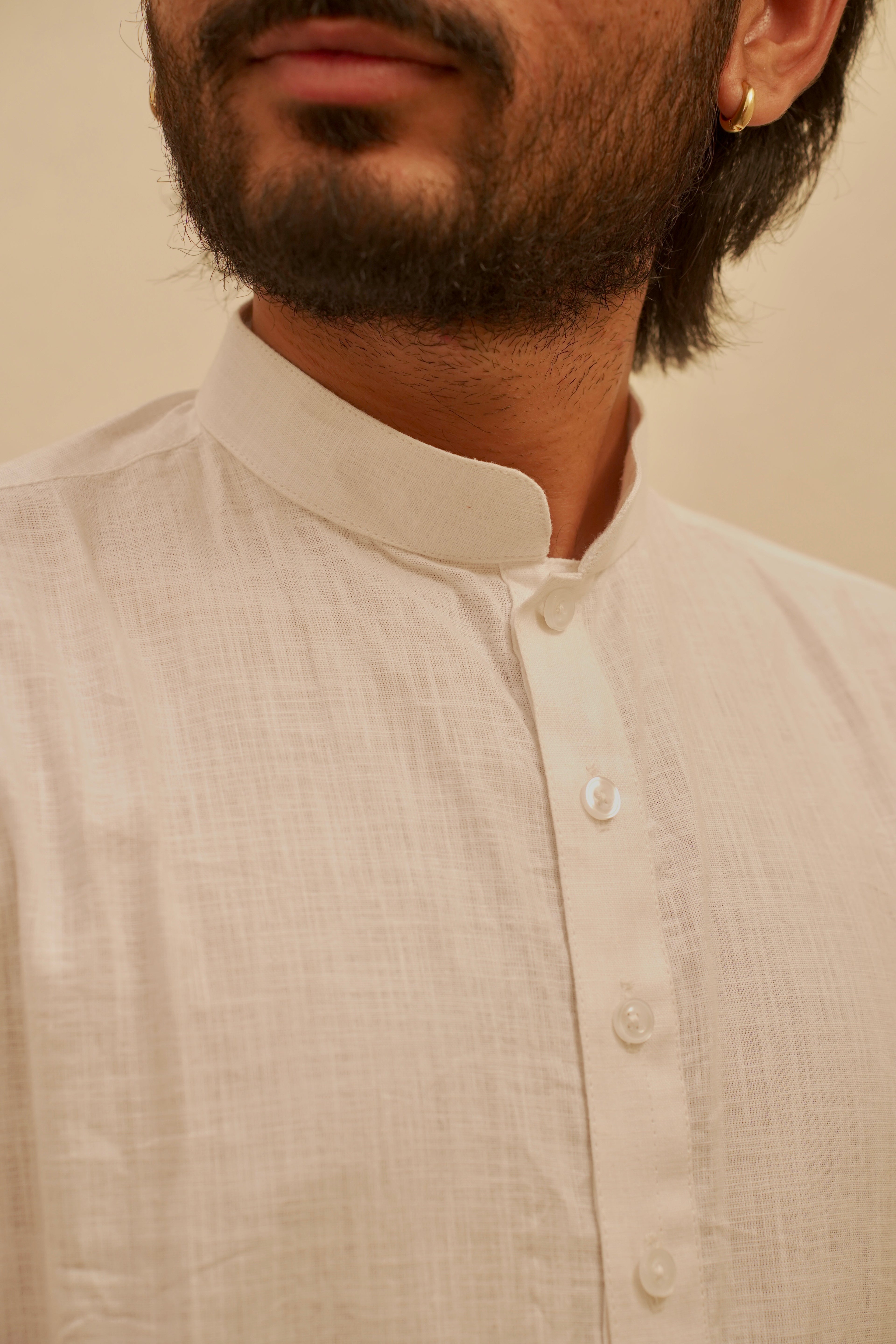 Close-up of a man wearing a White linen kurta with a stand-up collar and white buttons, set against a plain beige background.