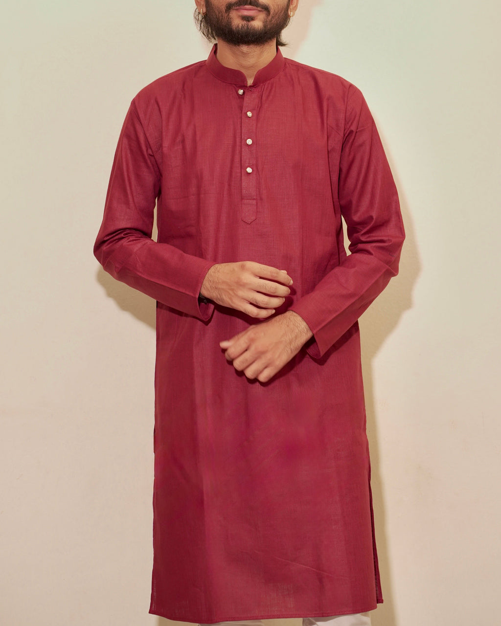 A man wearing a long-sleeved maroon kurta with a mandarin collar and a buttoned chest, standing against a plain light beige background.