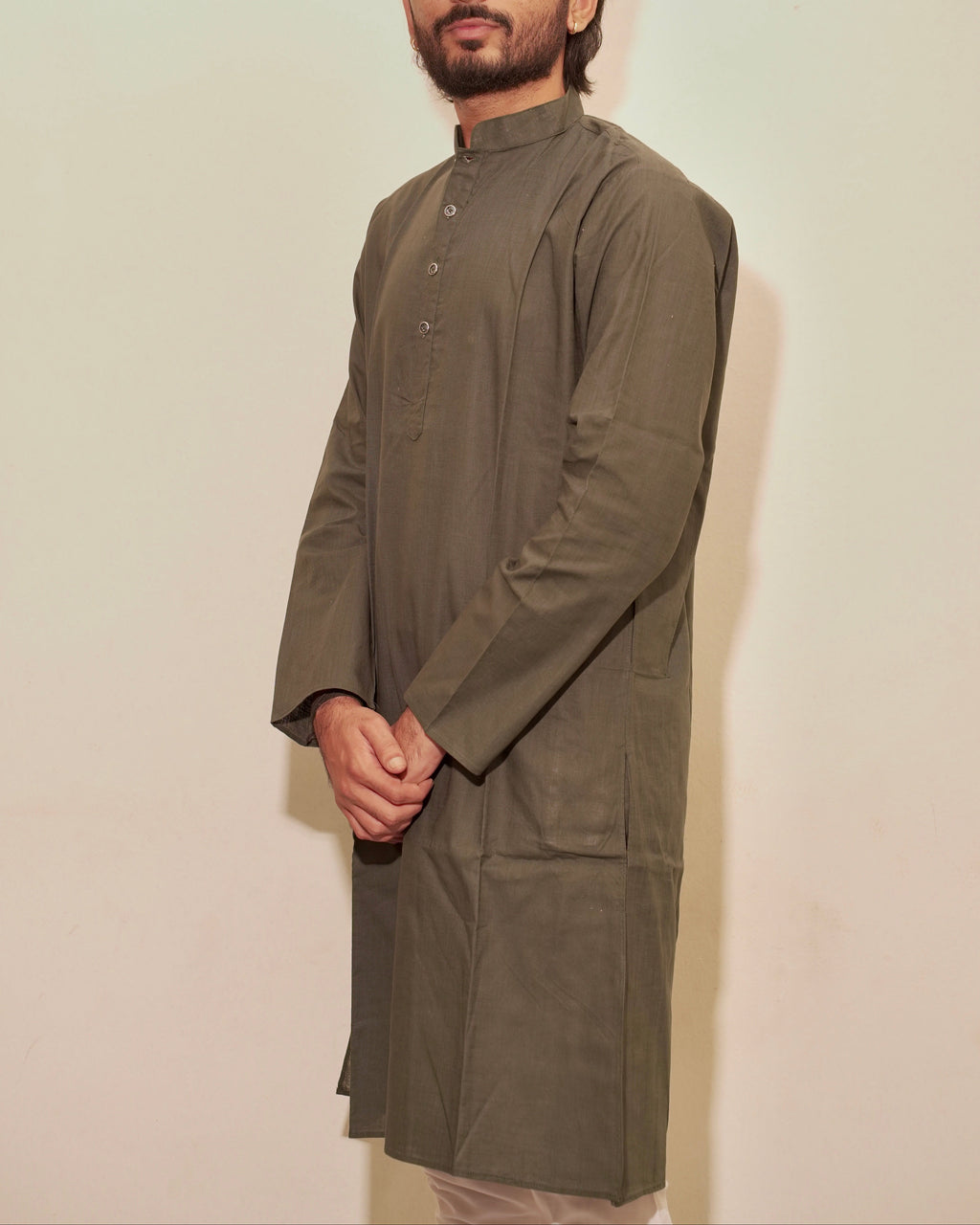 A man wearing a long-sleeved Bottle green kurta with a band collar and front buttons, paired with white pajama, standing against a plain off-white background.