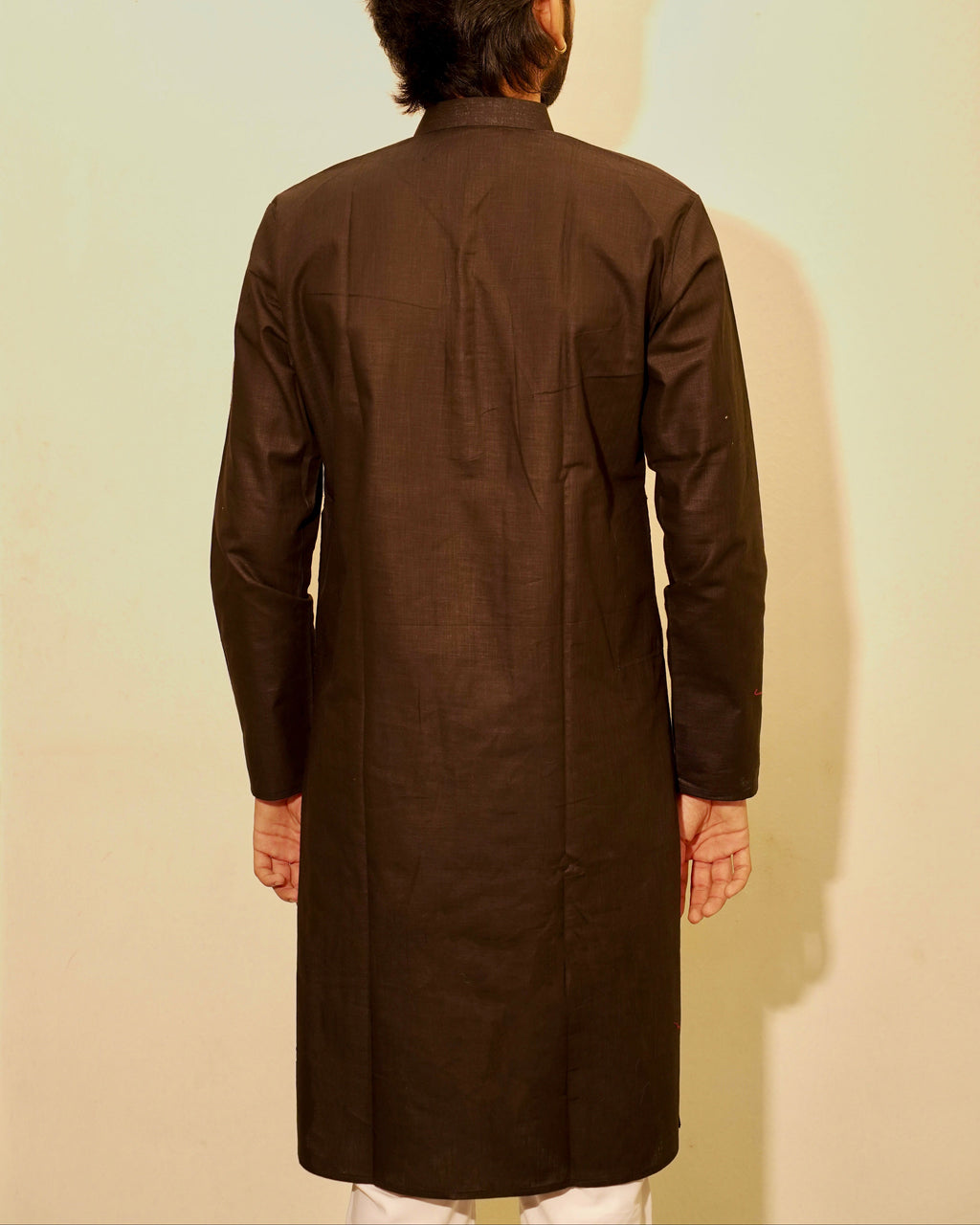 A man viewed from behind wearing a Black long-sleeved kurta against a plain light beige background.