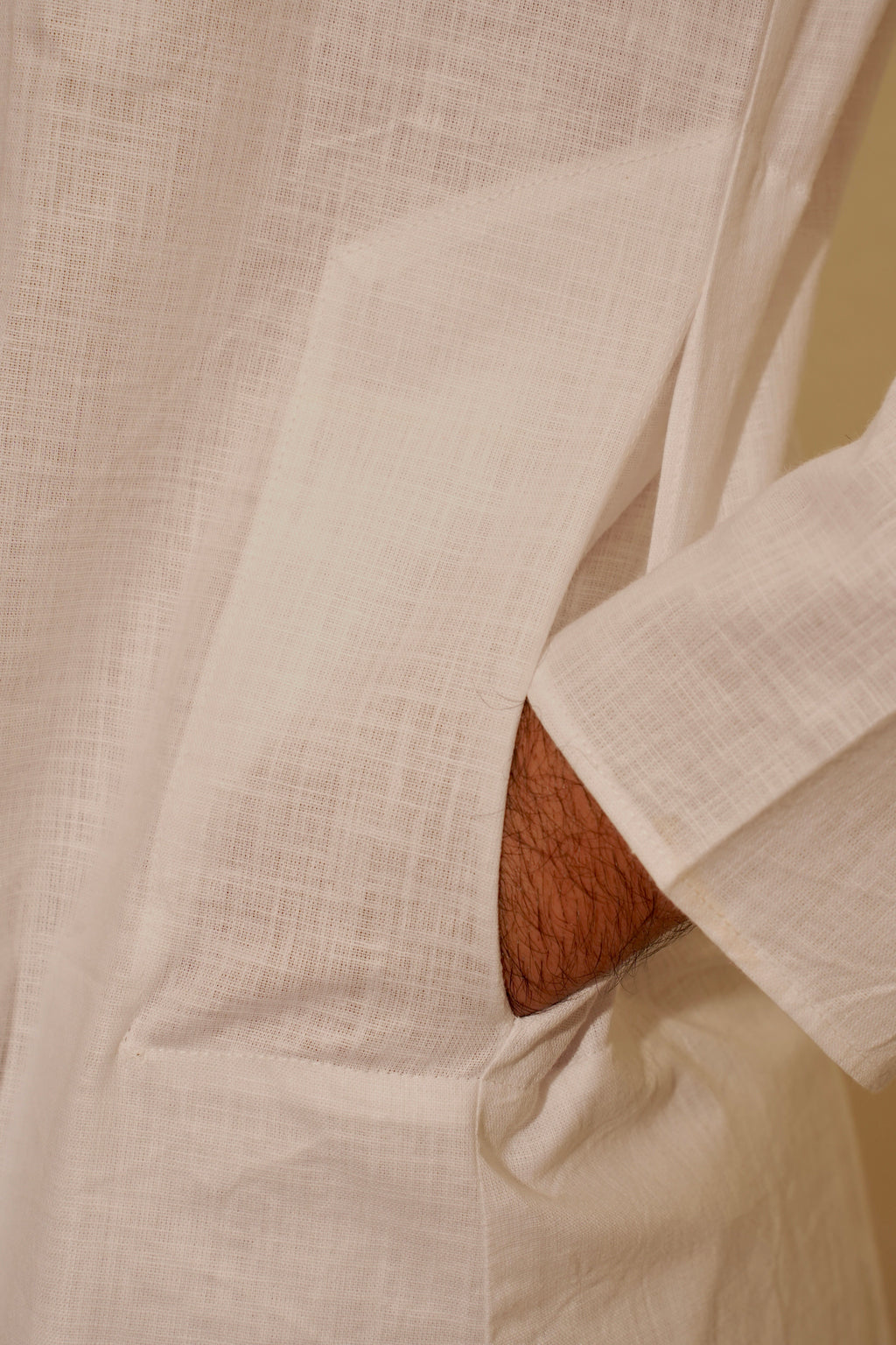 Close-up of a White linen Kurta with a textured weave, showing a pocket opening and a glimpse of a person's arm.