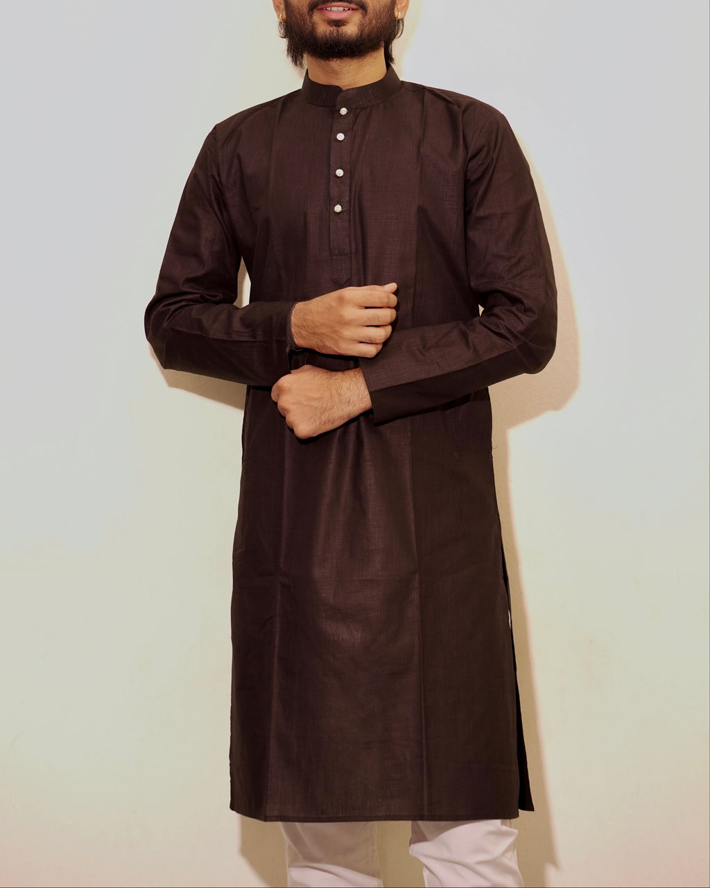A man wearing a Black long-sleeve kurta with a band collar and small front buttons, paired with white pajama, standing against a plain light background.