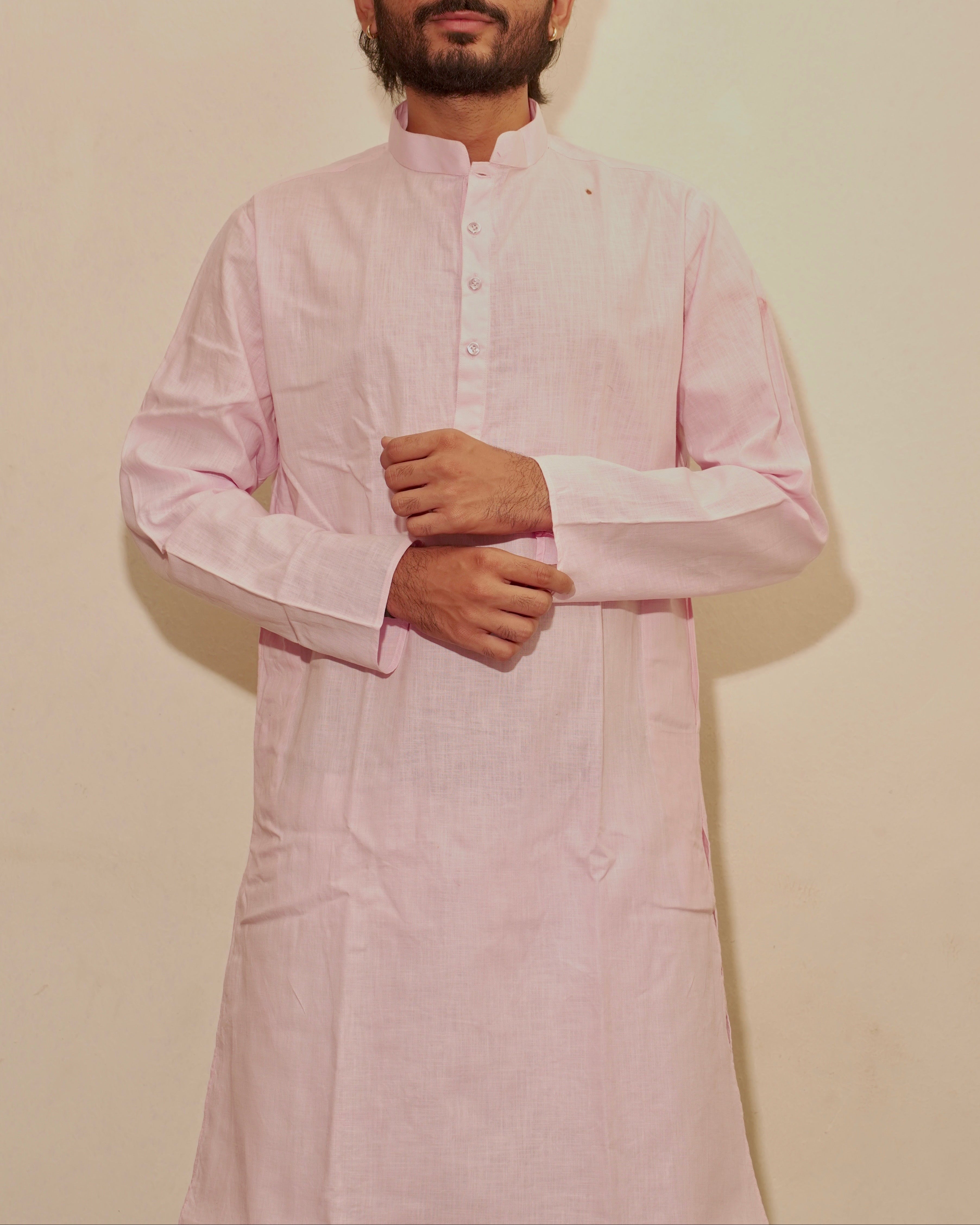 A man wearing a light pink long-sleeve kurta with a mandarin collar and buttoned front, standing against a plain beige wall.