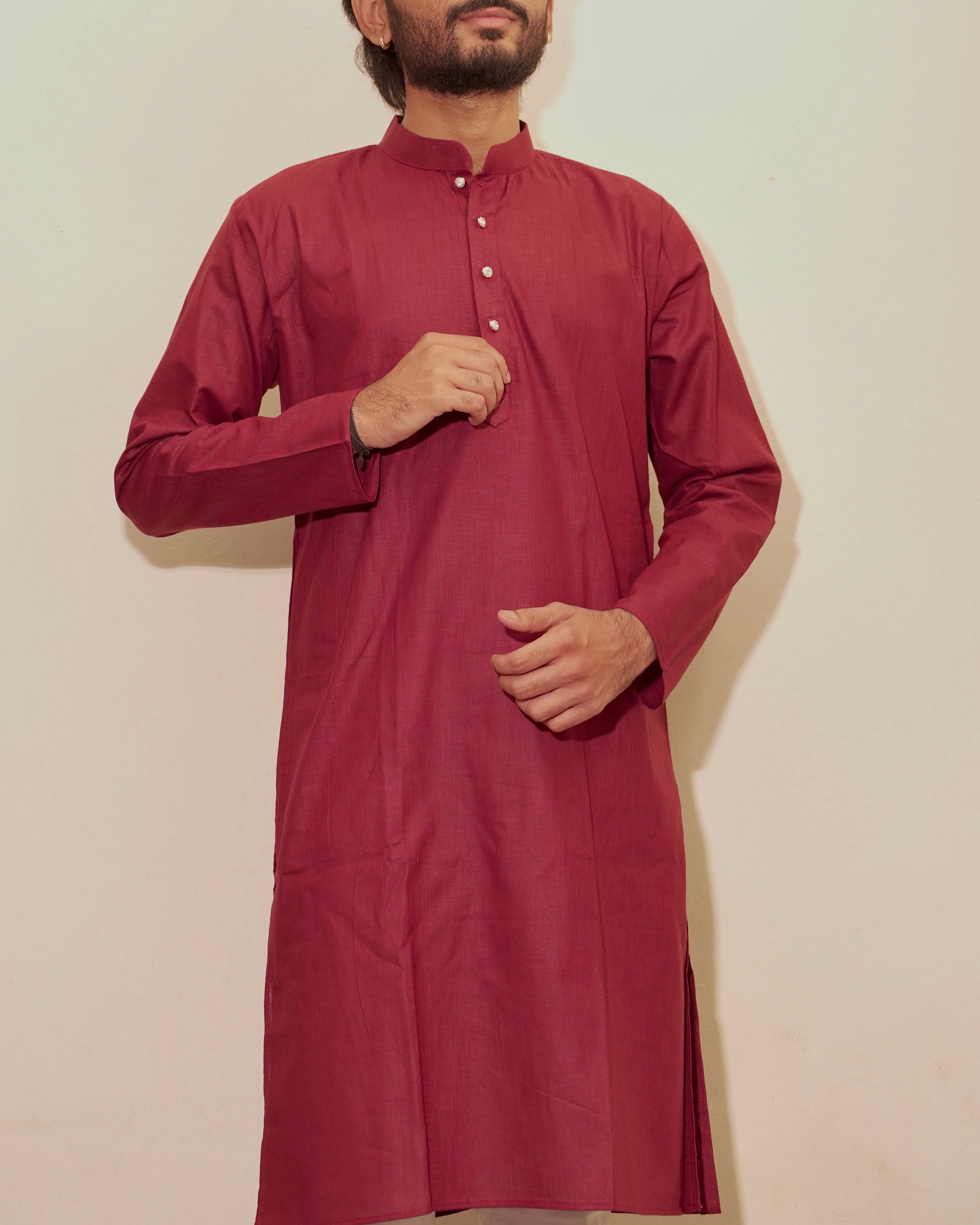 A man wearing a long-sleeved maroon kurta with a mandarin collar and a three-button placket, standing against a plain off-white background.