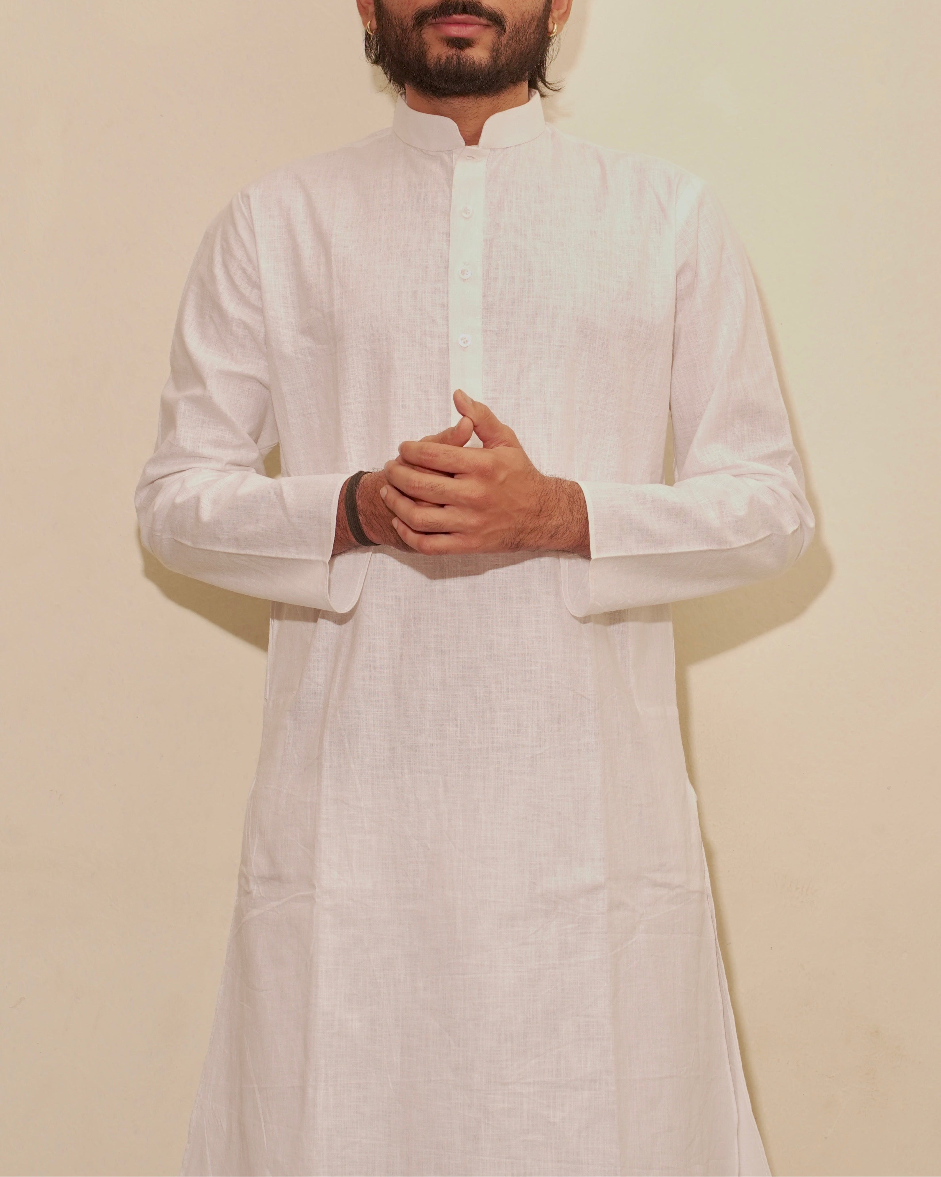 A man wearing a white long-sleeve kurta with a mandarin collar, standing against a plain beige background.