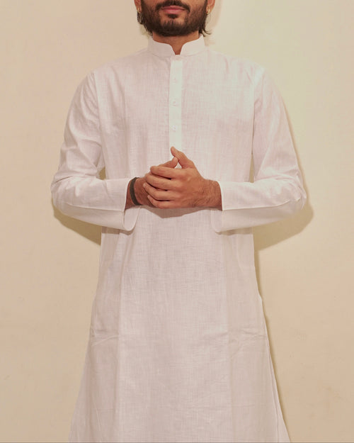 A man wearing a white long-sleeve kurta with a mandarin collar, standing against a plain beige background.