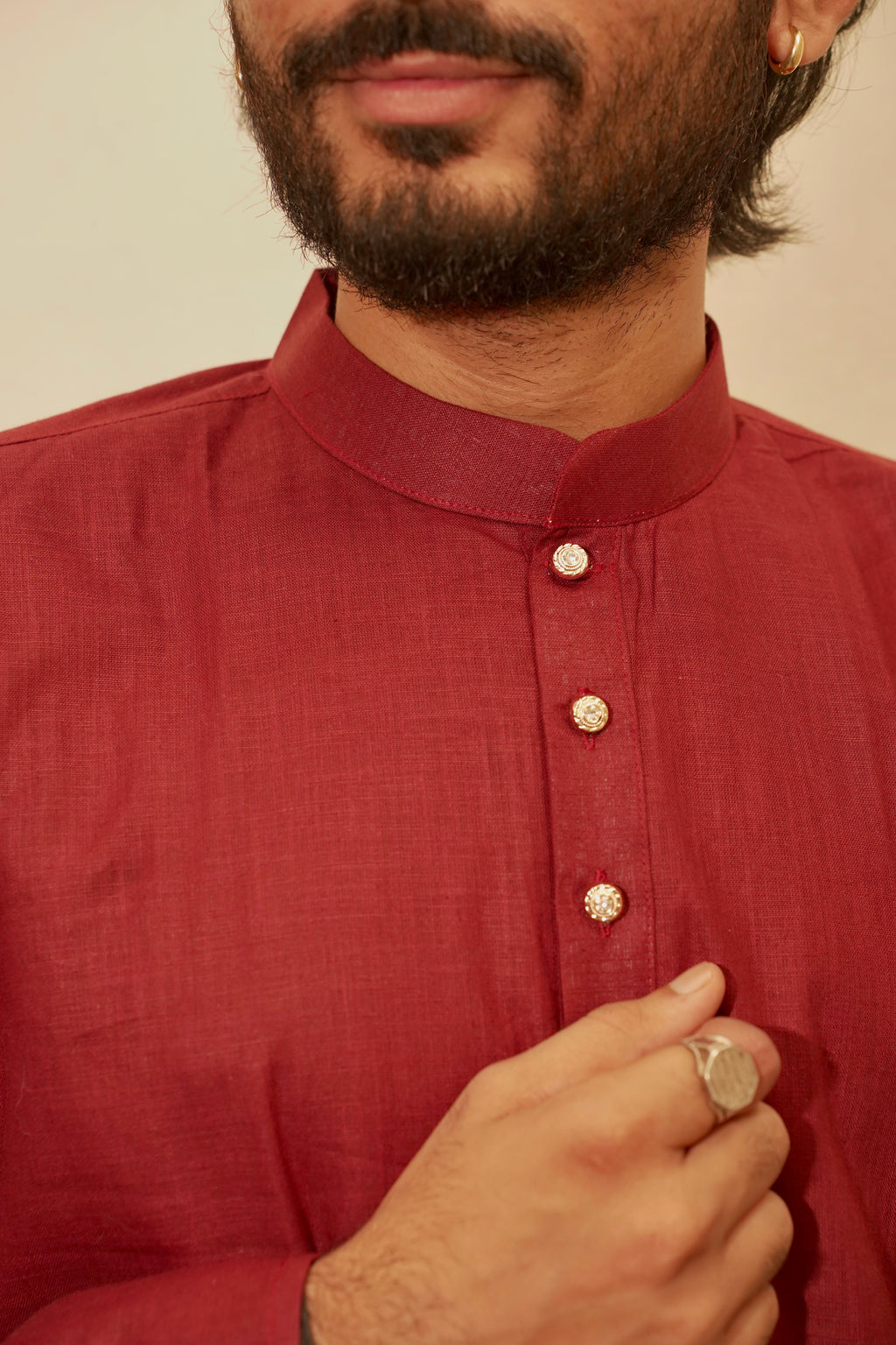 A close-up of a man wearing a maroon red linen kurta with a mandarin collar and decorative metallic buttons, with his hand adjusting the collar.