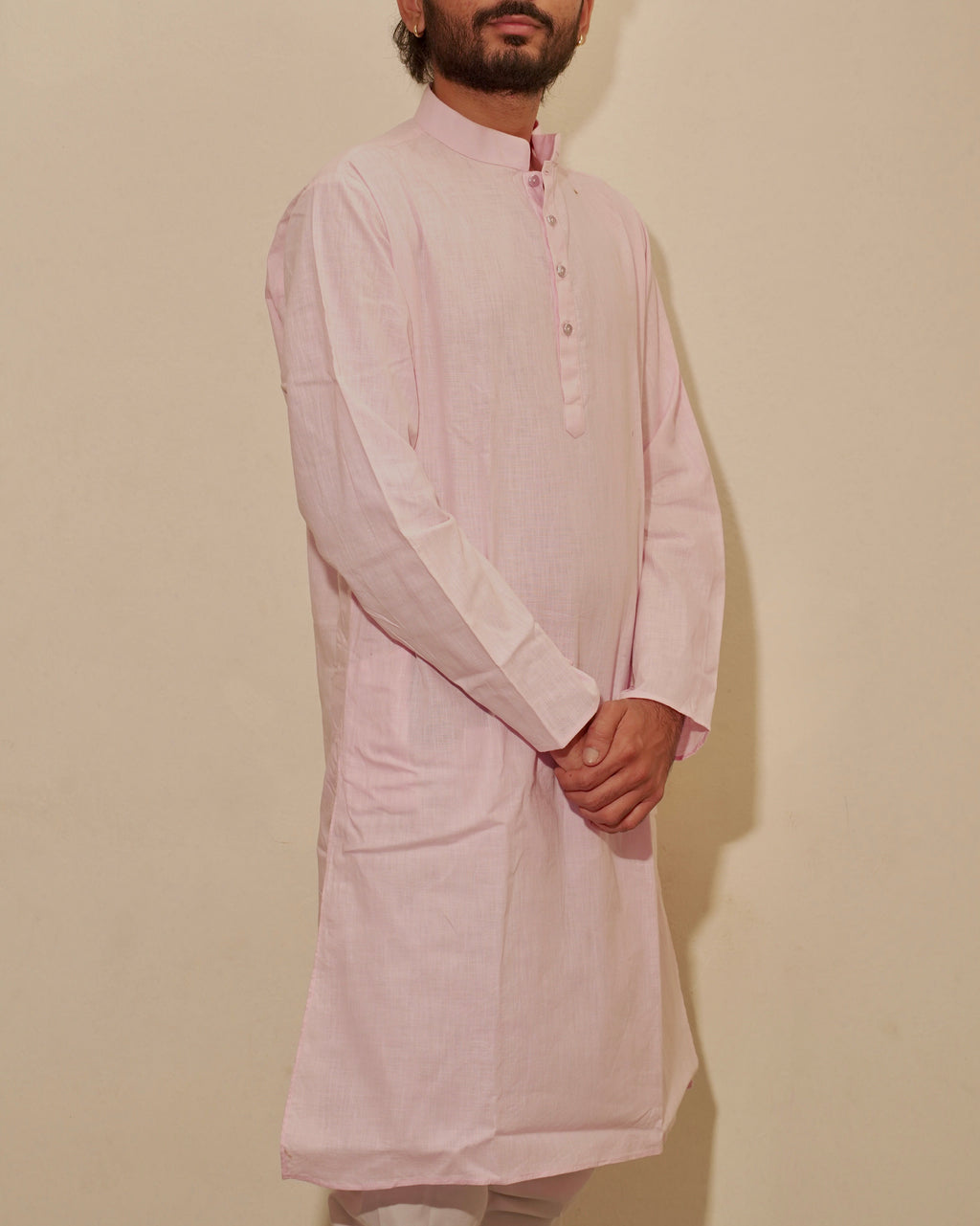 A man wearing a light pink long-sleeve kurta with a mandarin collar and button placket, paired with off-white pajama, standing against a plain beige wall.