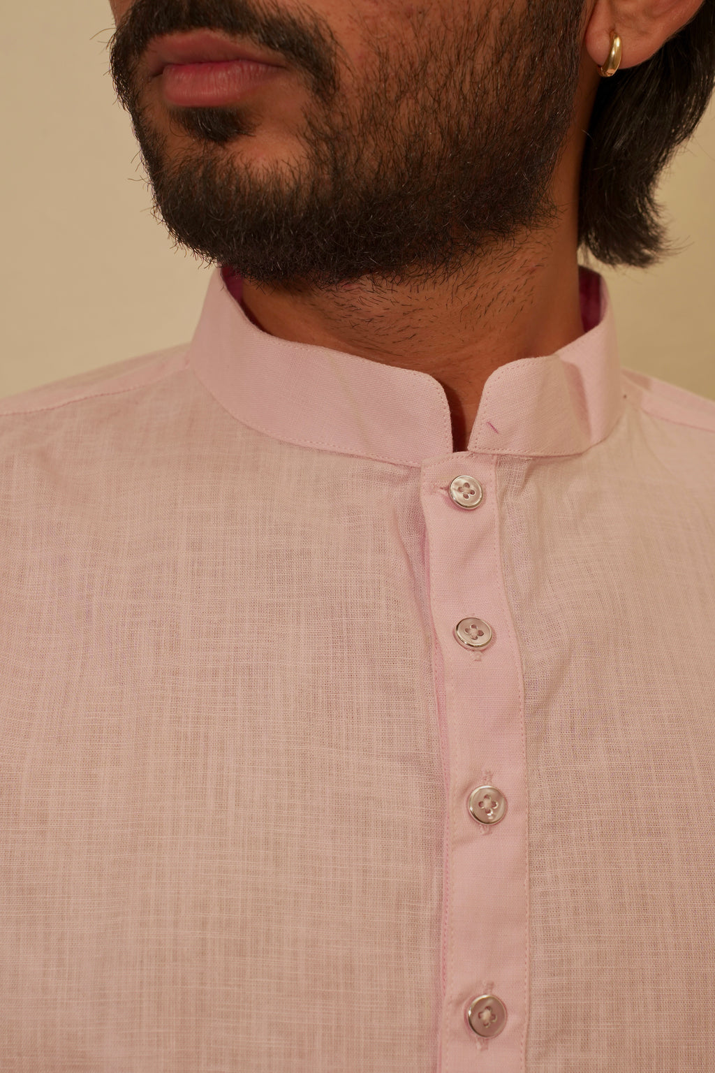 Close-up of a man wearing a light pink linen kurta with a mandarin collar and silver buttons, set against a plain beige background.