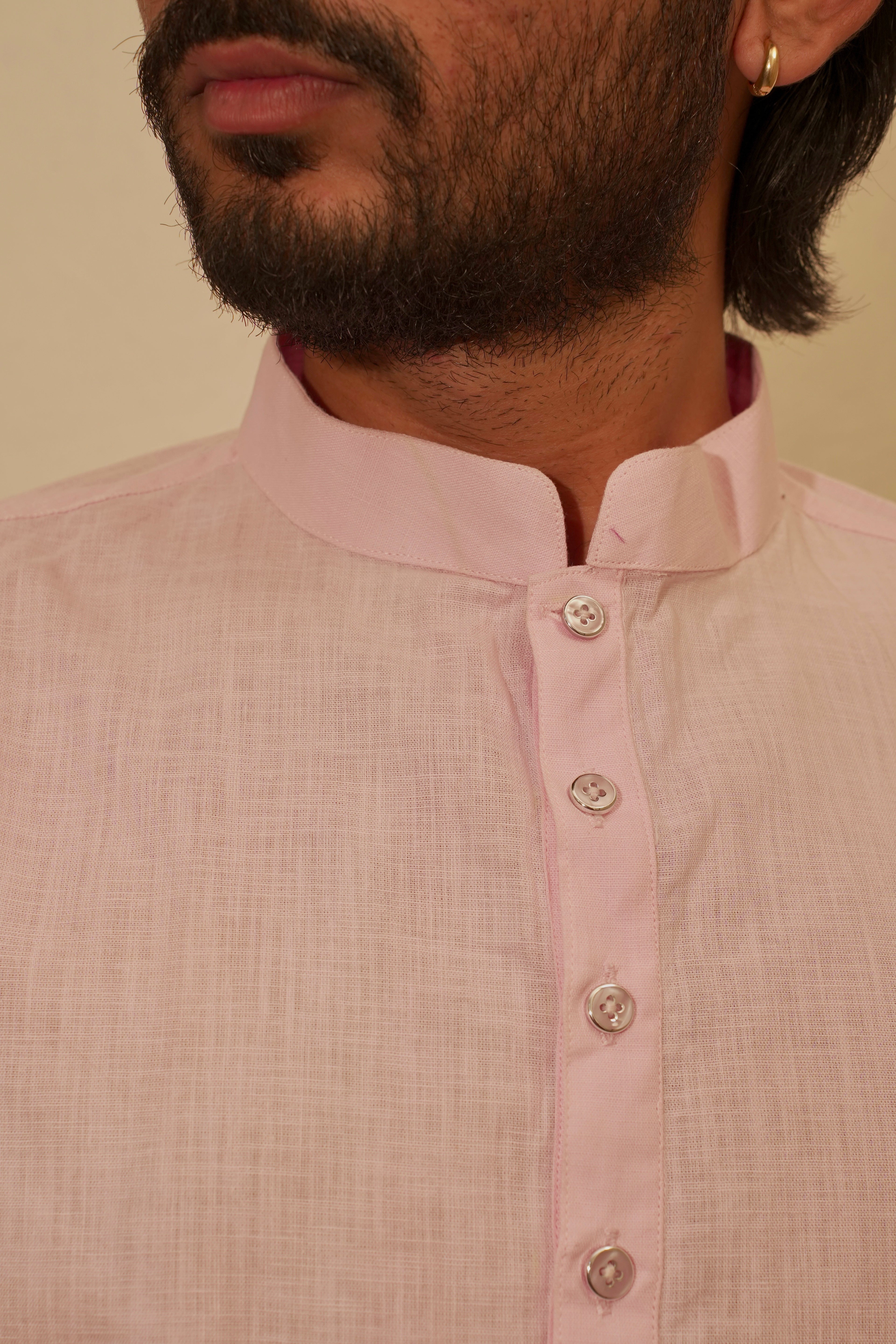 Close-up of a man wearing a light pink linen kurta with a mandarin collar and silver buttons, set against a plain beige background.