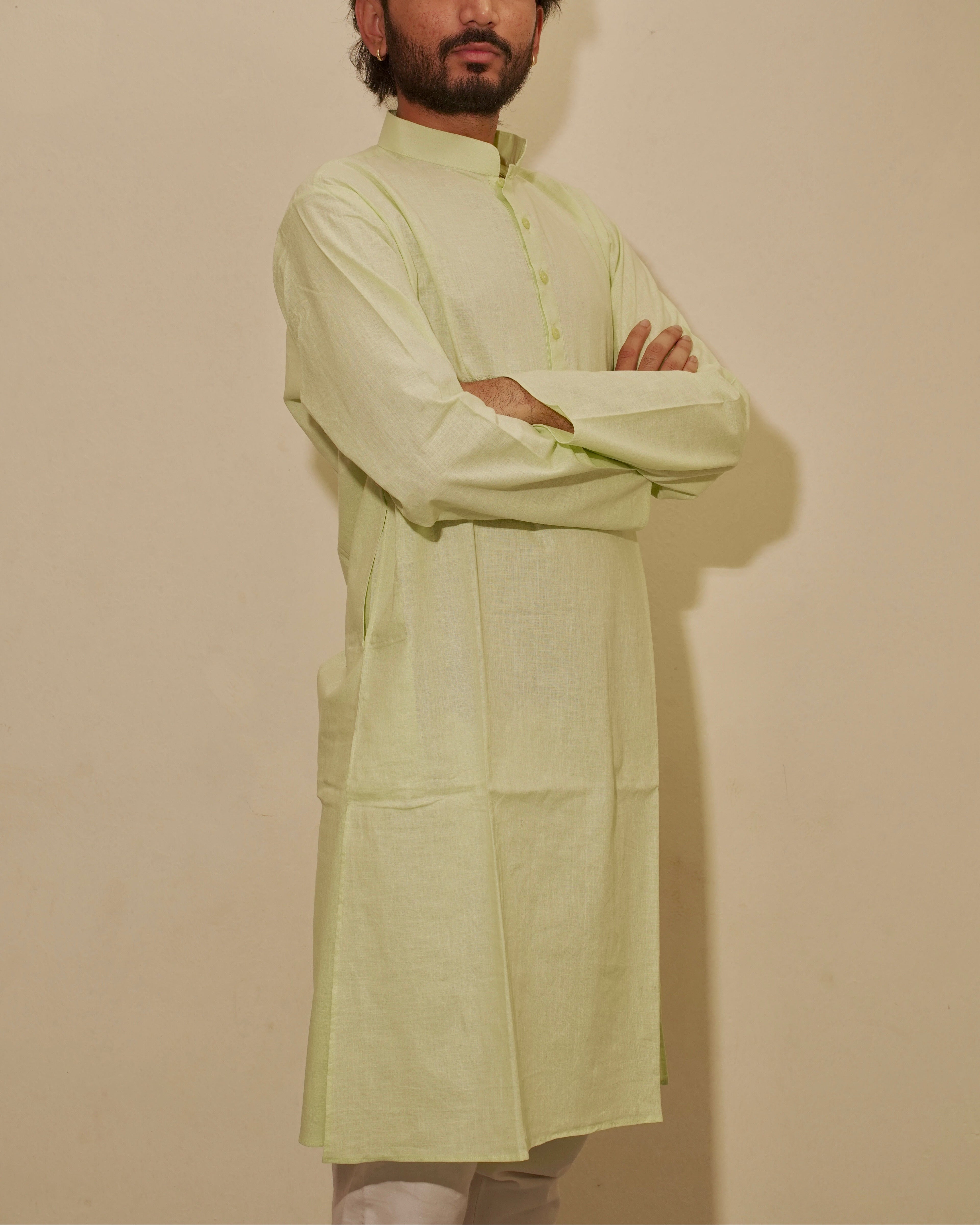 A man wearing a light lime green long-sleeve kurta with a mandarin collar, standing with arms crossed against a plain beige wall.