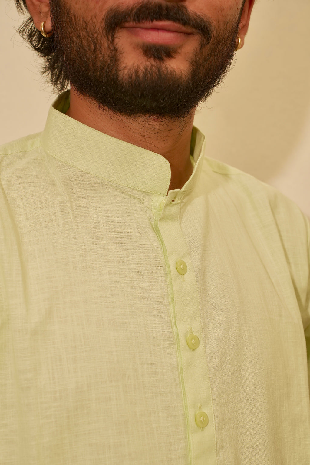 Close-up of a man wearing a Lime green linen kurta with a mandarin collar and matching buttons, set against a plain beige background.