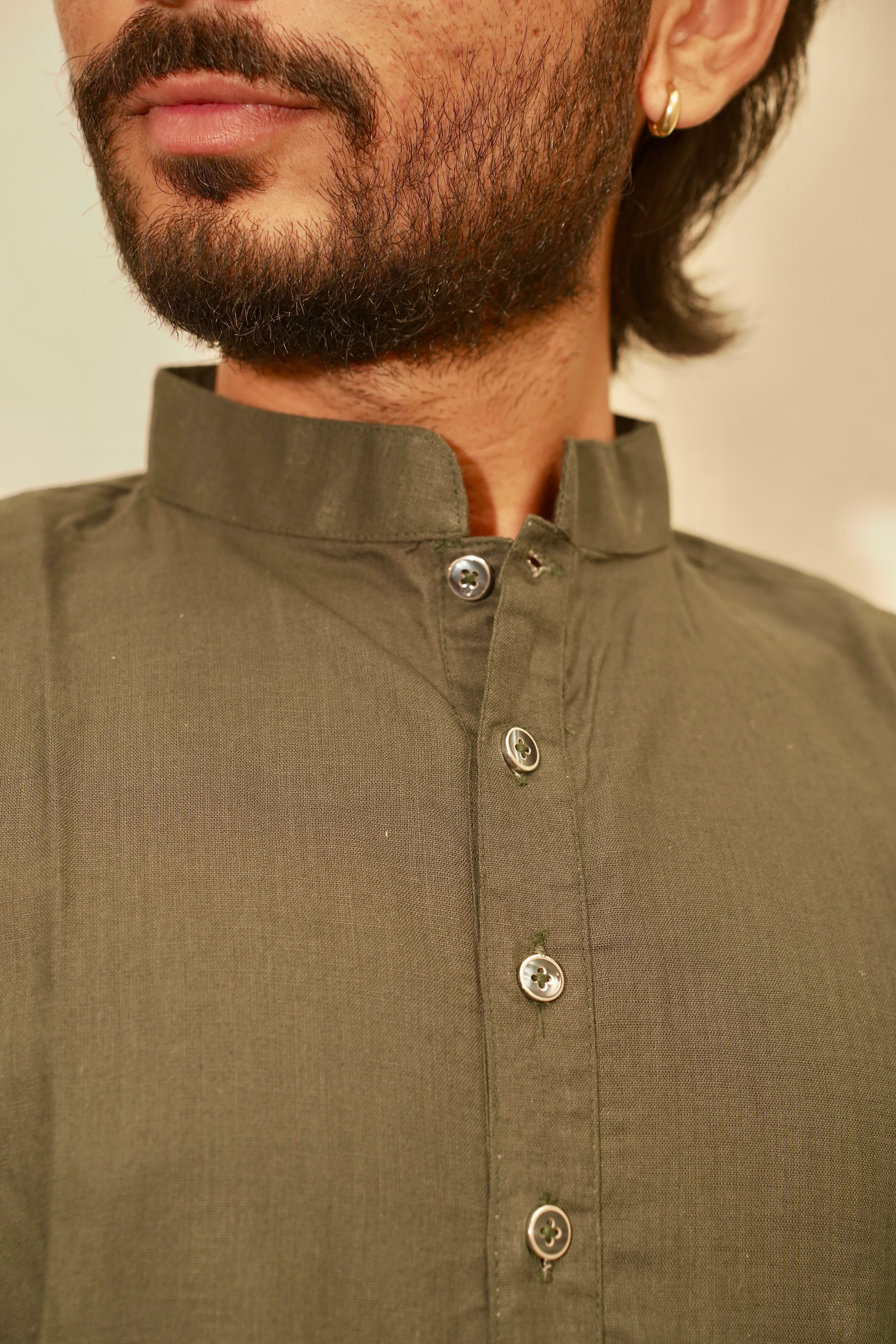 Close-up of a man wearing an Bottle green linen shirt with a mandarin collar and silver buttons.